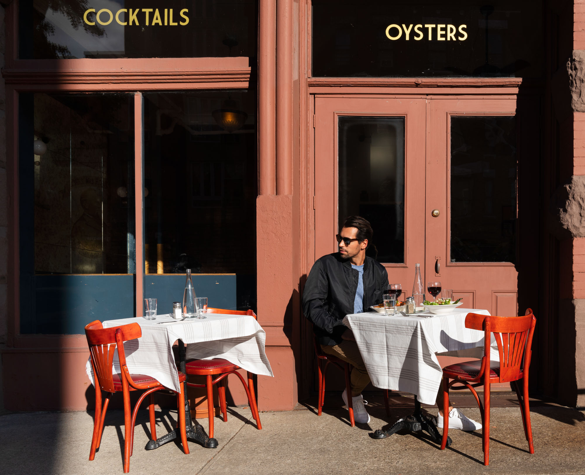 A man sits outside a restaurant that serves cocktails and oysters in Greenpoint, Brooklyn near Two Blue Slip apartments.