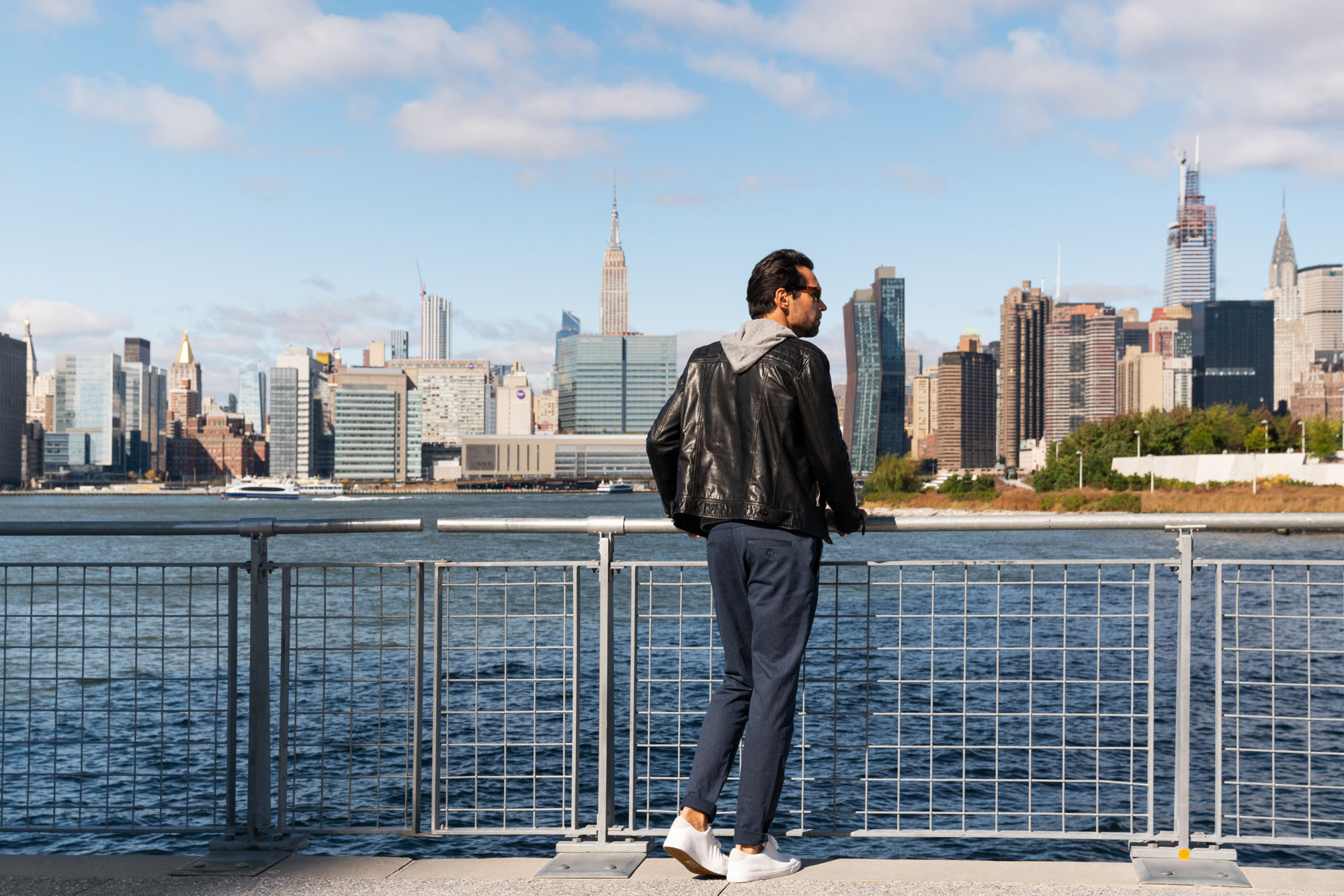 A man stands along the Greenpoint waterfront overlooking the Manhattan skyline near Two Blue Slip apartments.