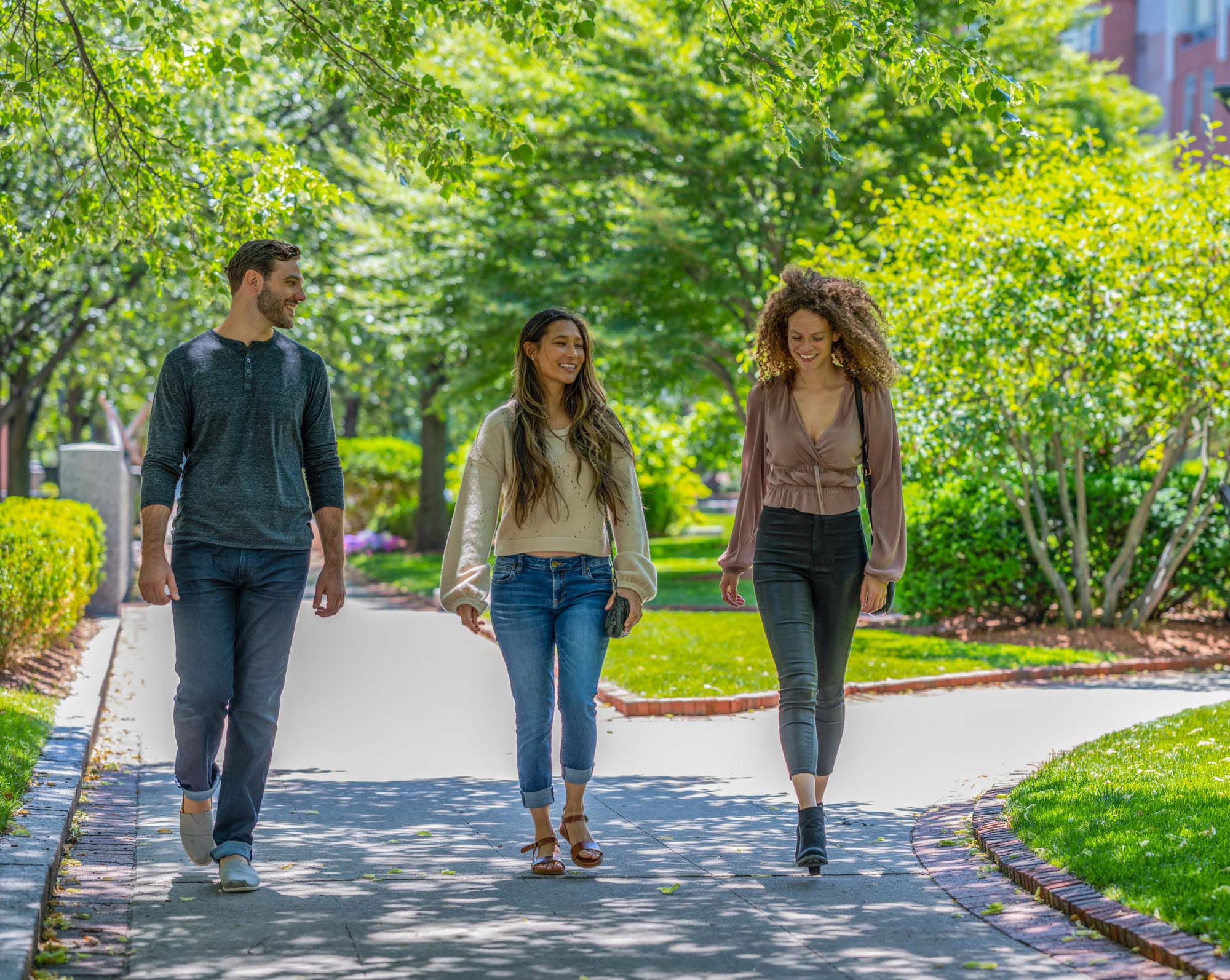 Three friends enjoy a walk around the neighborhood amidst a vibrant green backdrop.